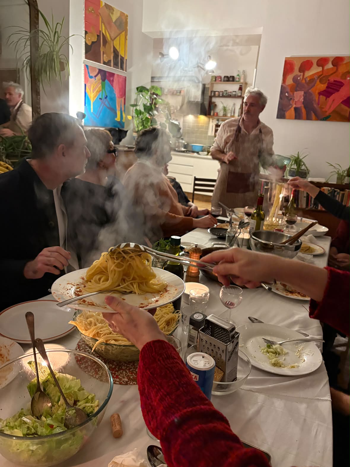 Guests sharing spaghetti at Spaghetti Soirée No. 2, with paintings in the dining room